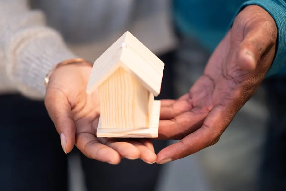 Hands holding a small wooden house model, symbolizing new home ownership and real estate transactions.