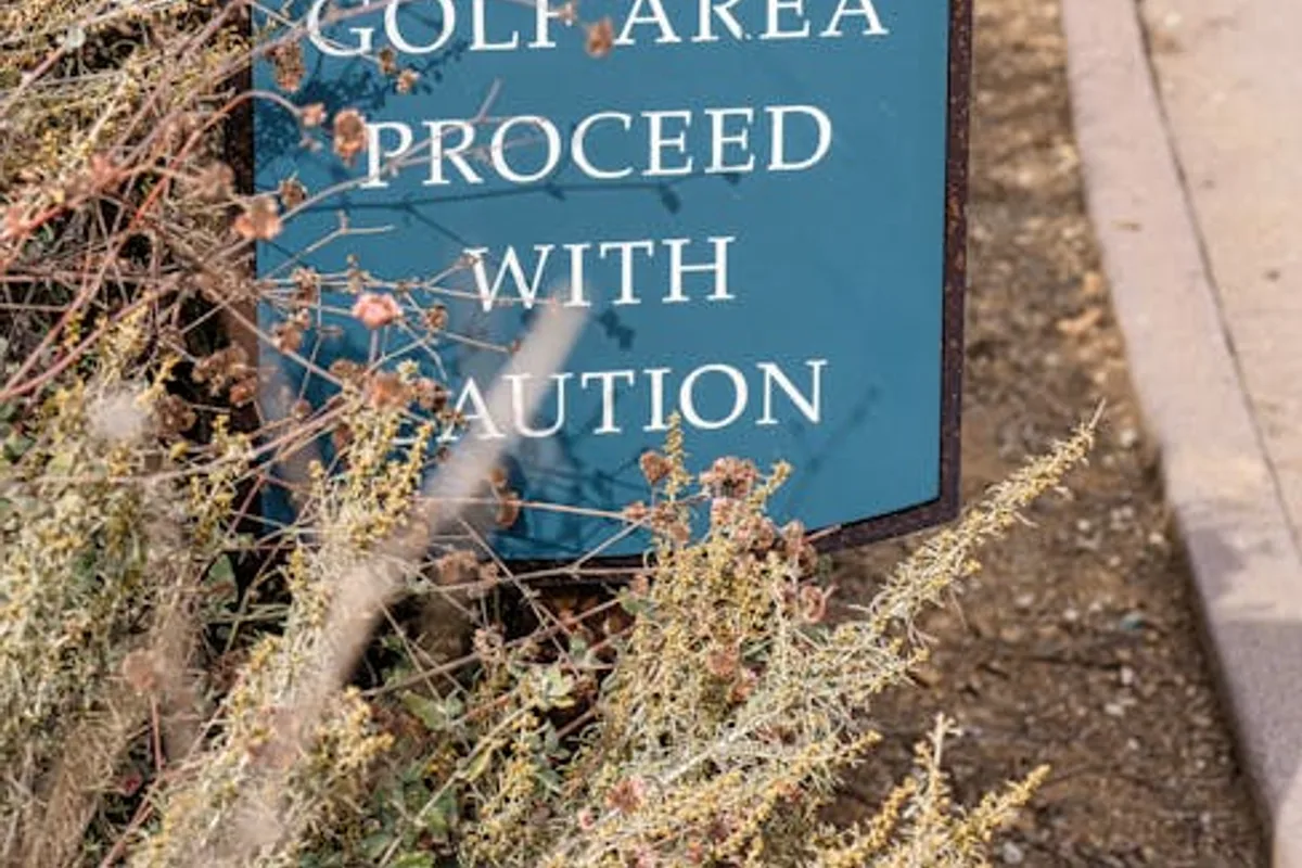 Sign in a golf park warns to proceed with caution, surrounded by foliage.