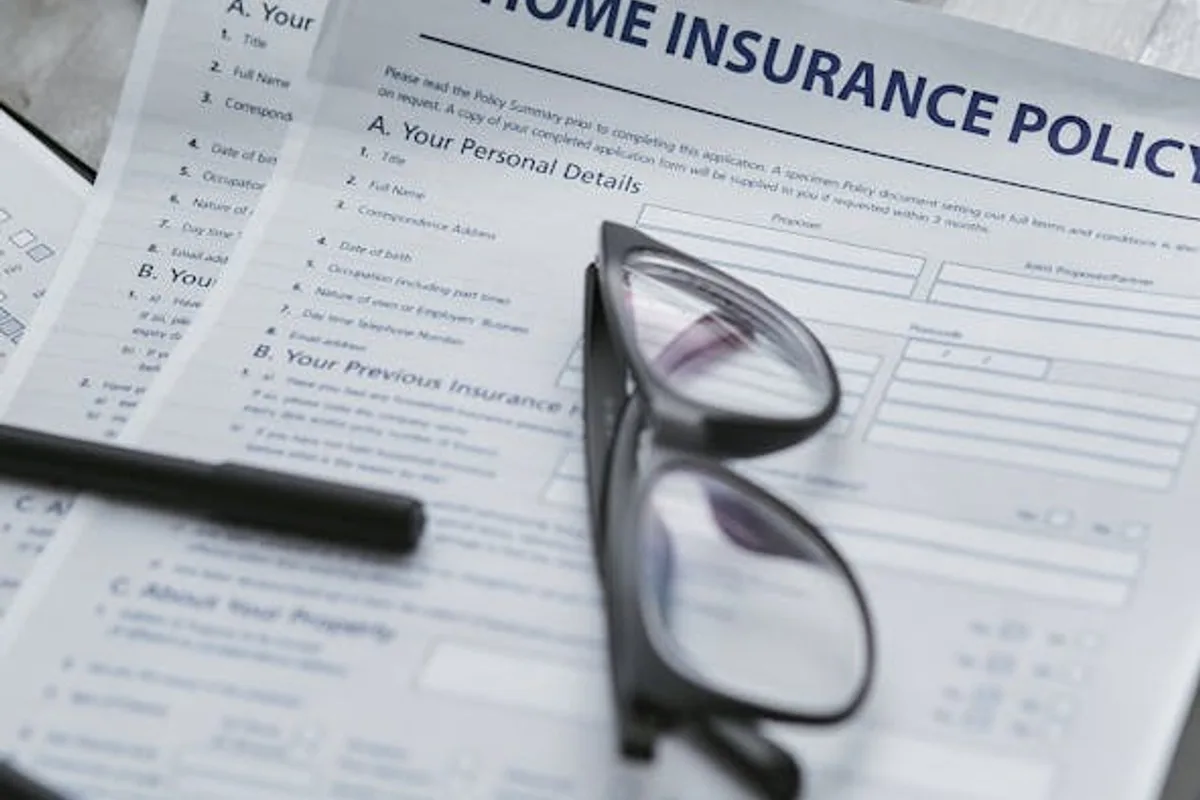 Close-up of home insurance policy document with glasses and laptop on a table.