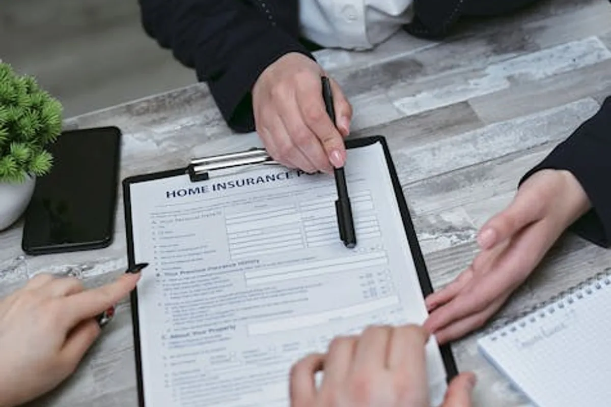 An agent and clients discussing paperwork for home insurance at a meeting table.