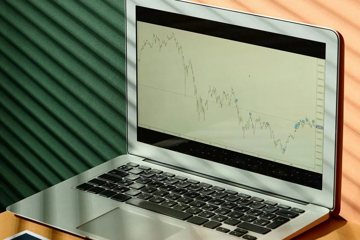 A laptop displaying financial graphs with documents on a sunlit office desk, ideal for finance themes.