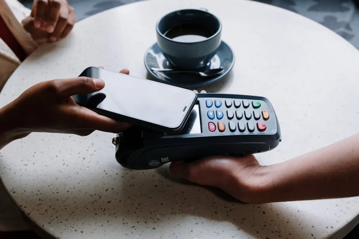 A person using a smartphone to make a contactless payment with a card reader on a cafe table.