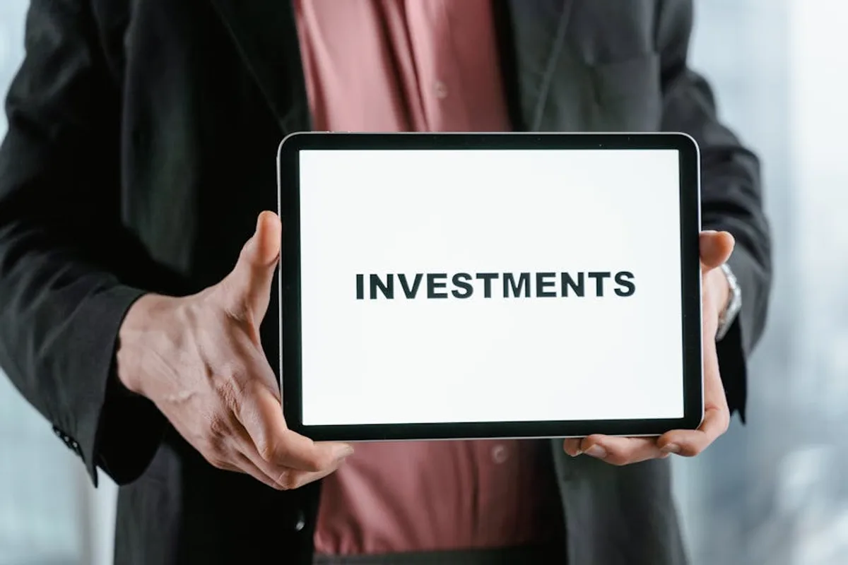 A businessman in a suit holds a tablet displaying the text 'INVESTMENTS'.