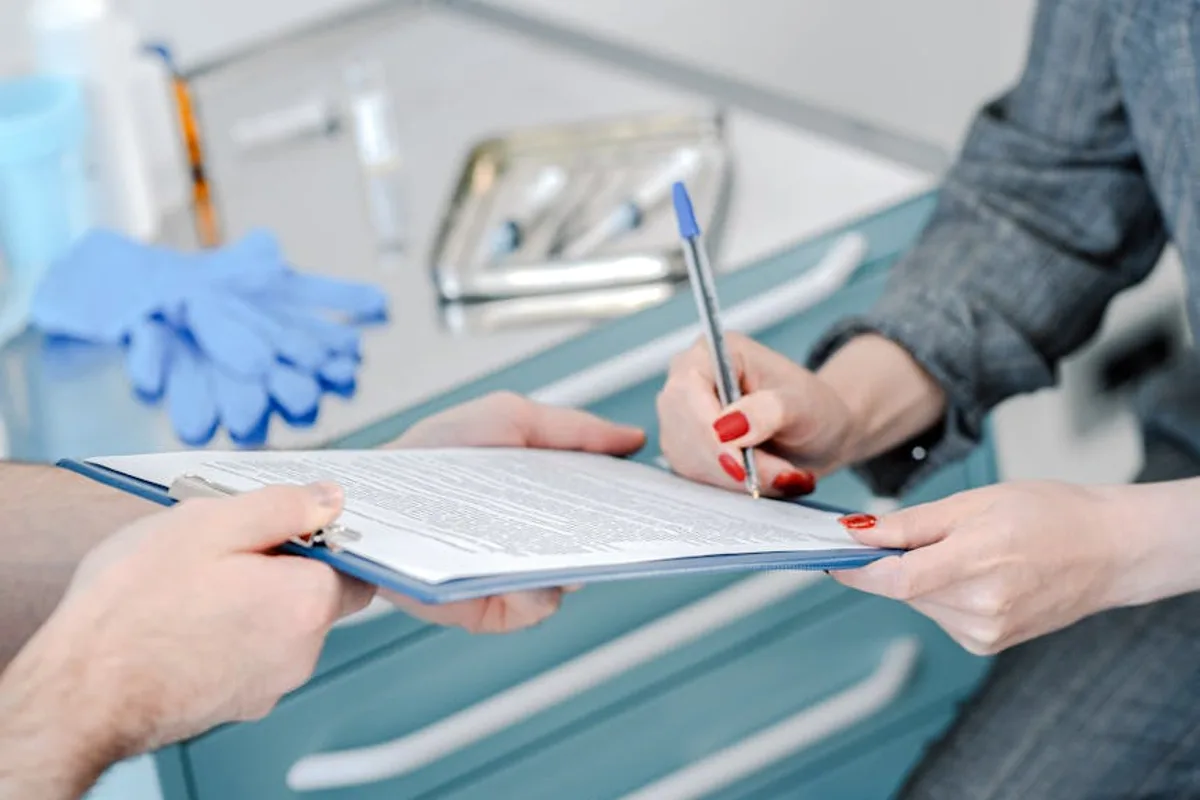 Patient signing healthcare agreement in doctor's office, focus on hands and document exchange.